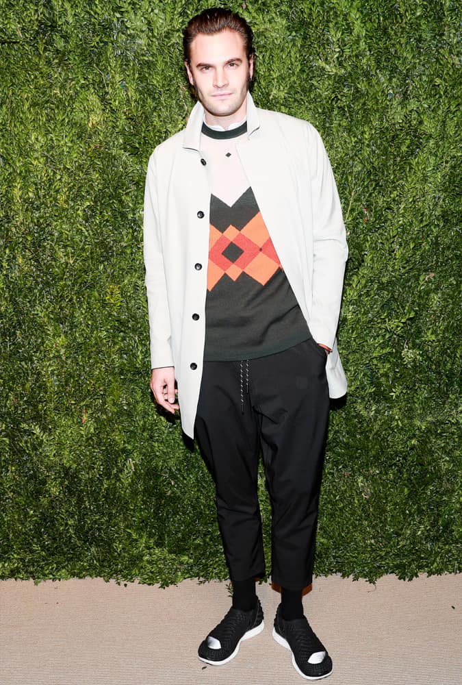 Tom Bateman wearing a white coat and knitwear
