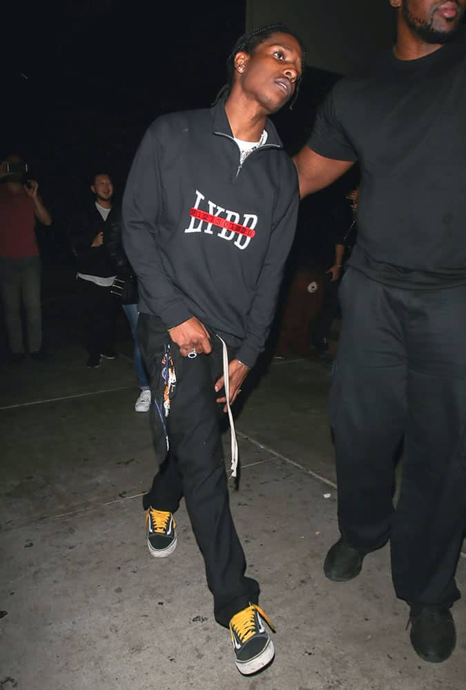 A$AP Rocky dressed in a zip-up sweatshirt and black trousers