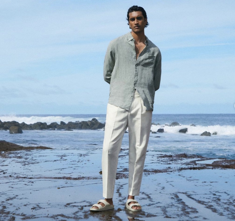 Man standing on a beach dressed in white slacks and a button t-shirt