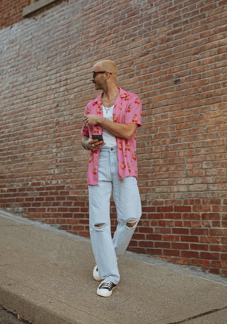 Man looking away from the camera wearing an open pink button-up and ripped jeans 