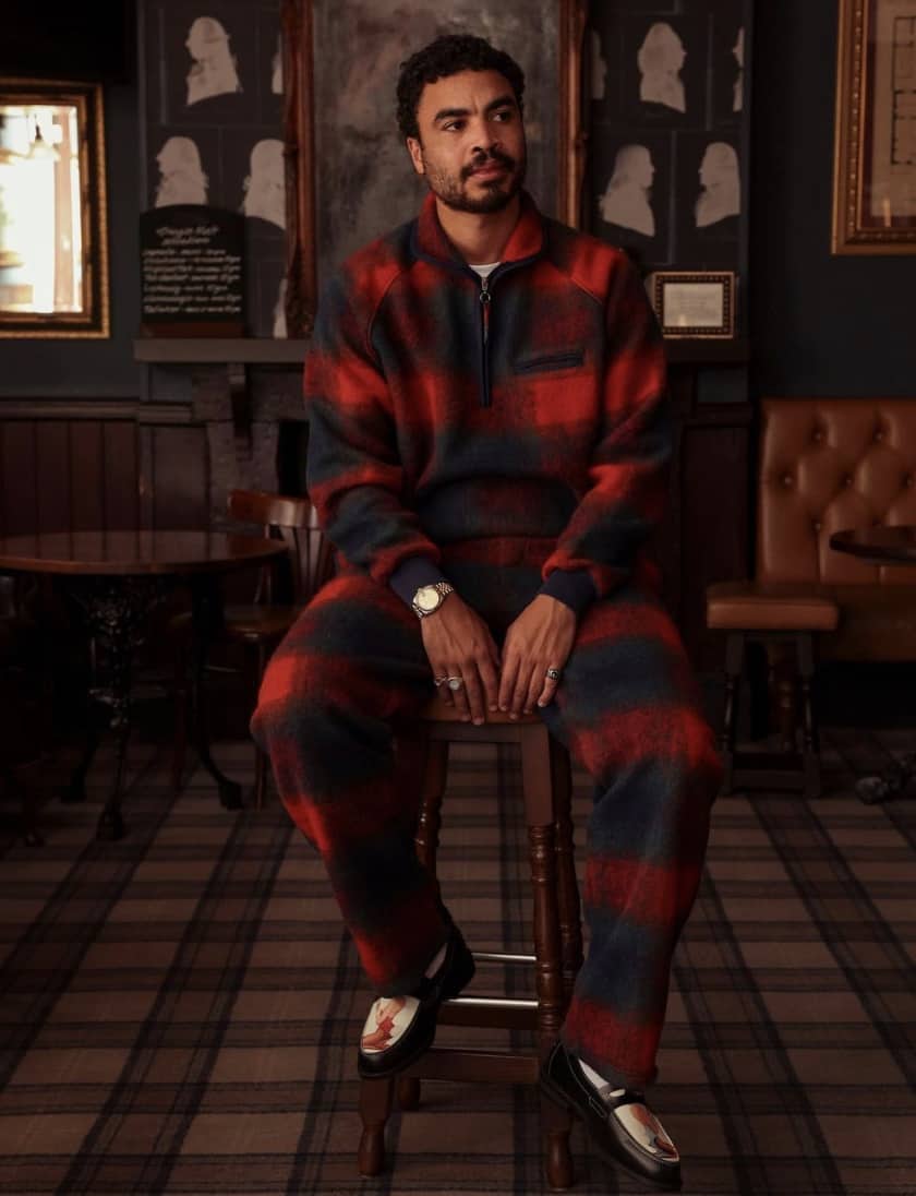 Man wearing matching plaid sweater and pants from Percival menswear, sitting in a chair
