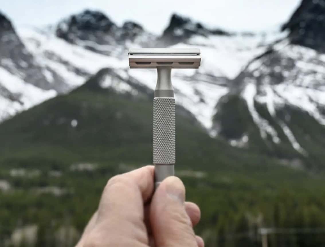man holding up a safety razor with mountains in the background