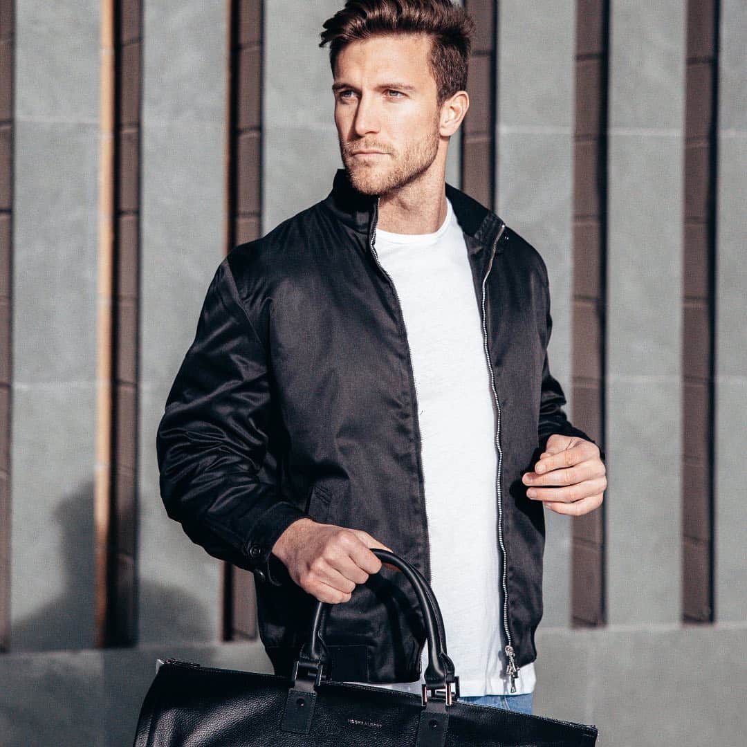 man in a bomber jacket carrying a leather weekend bag