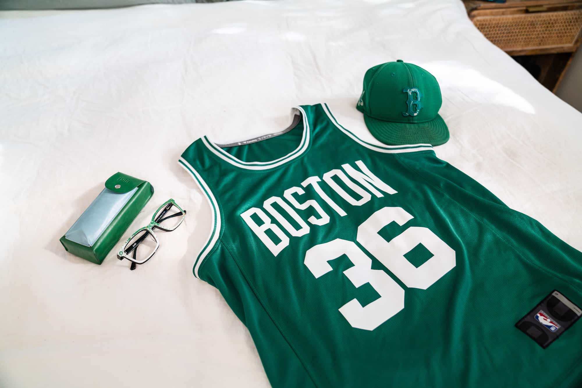 flat lay of a Boston Celtics jersey, a green hat and green glasses