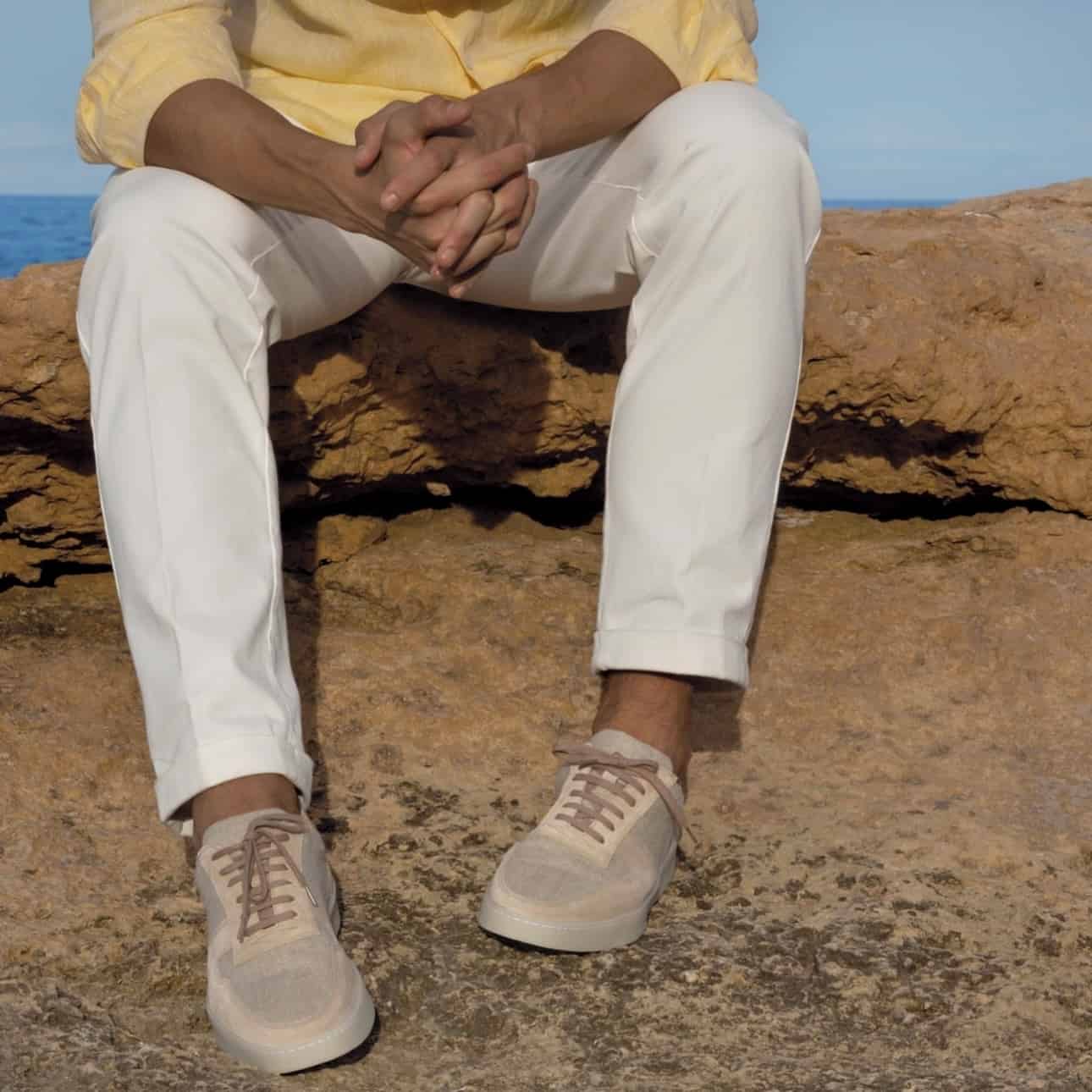 man sitting on a rock by the sea wearing a pair of aurelien sneakers