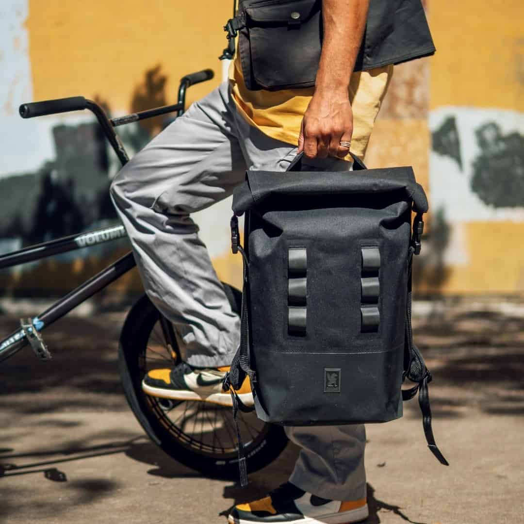 man carrying a black roll top backpack