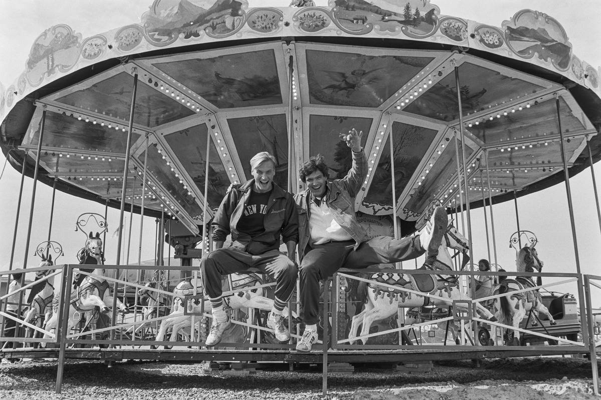 Two men in 1980s sitting on a merry go round fence