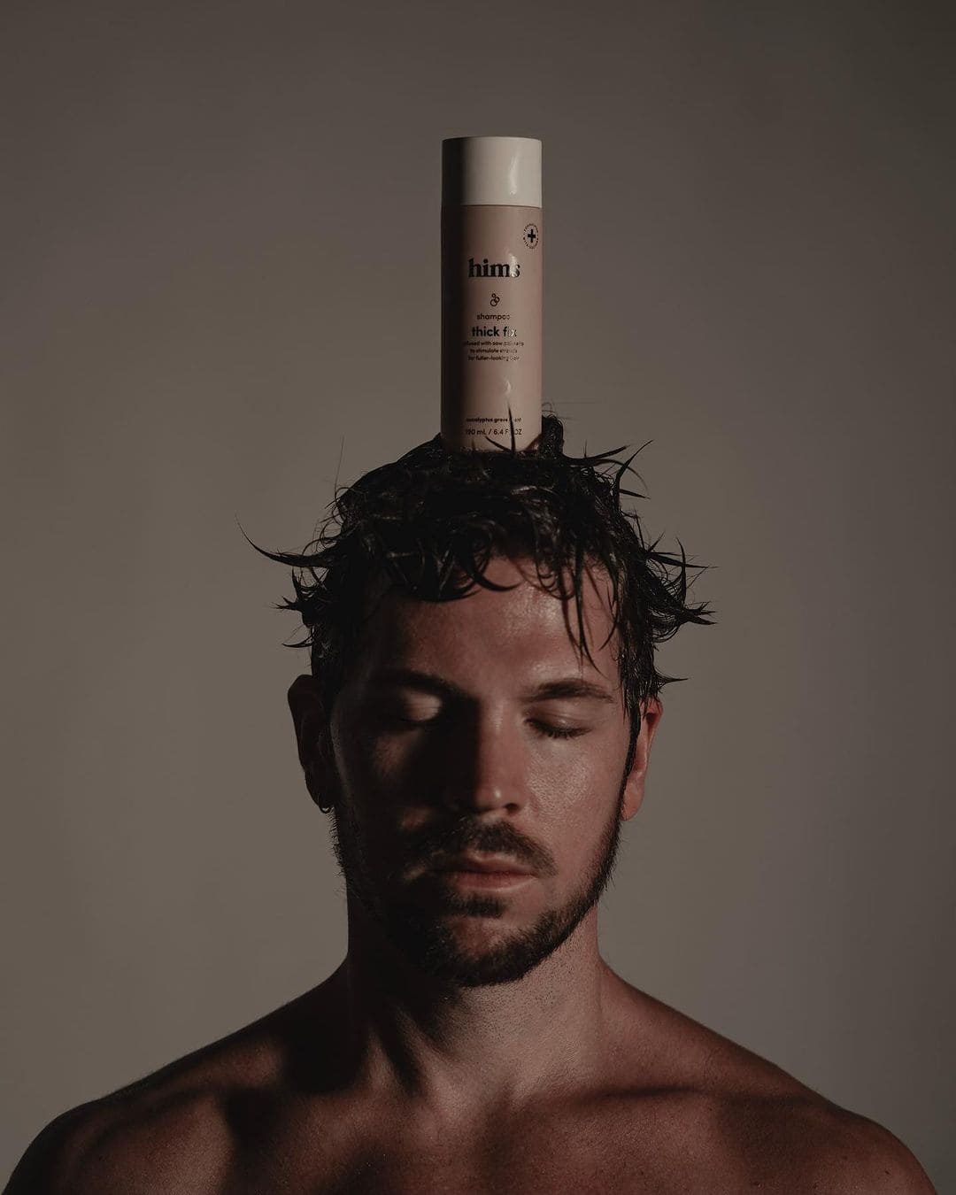 a bottle of thick fix shampoo by hims on top of a mans head