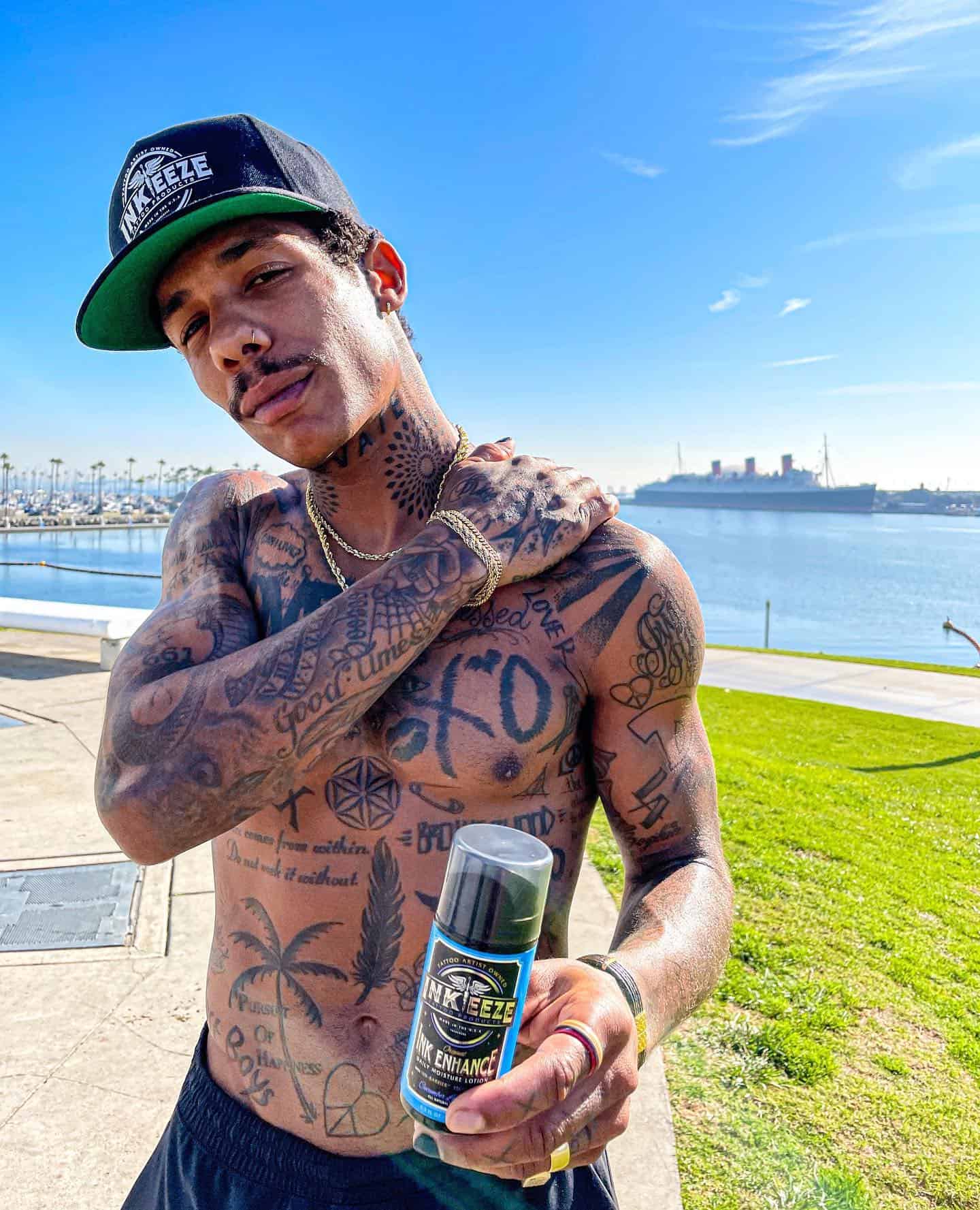 shirtless man with body tattoo holding a bottle of skin moisturizer