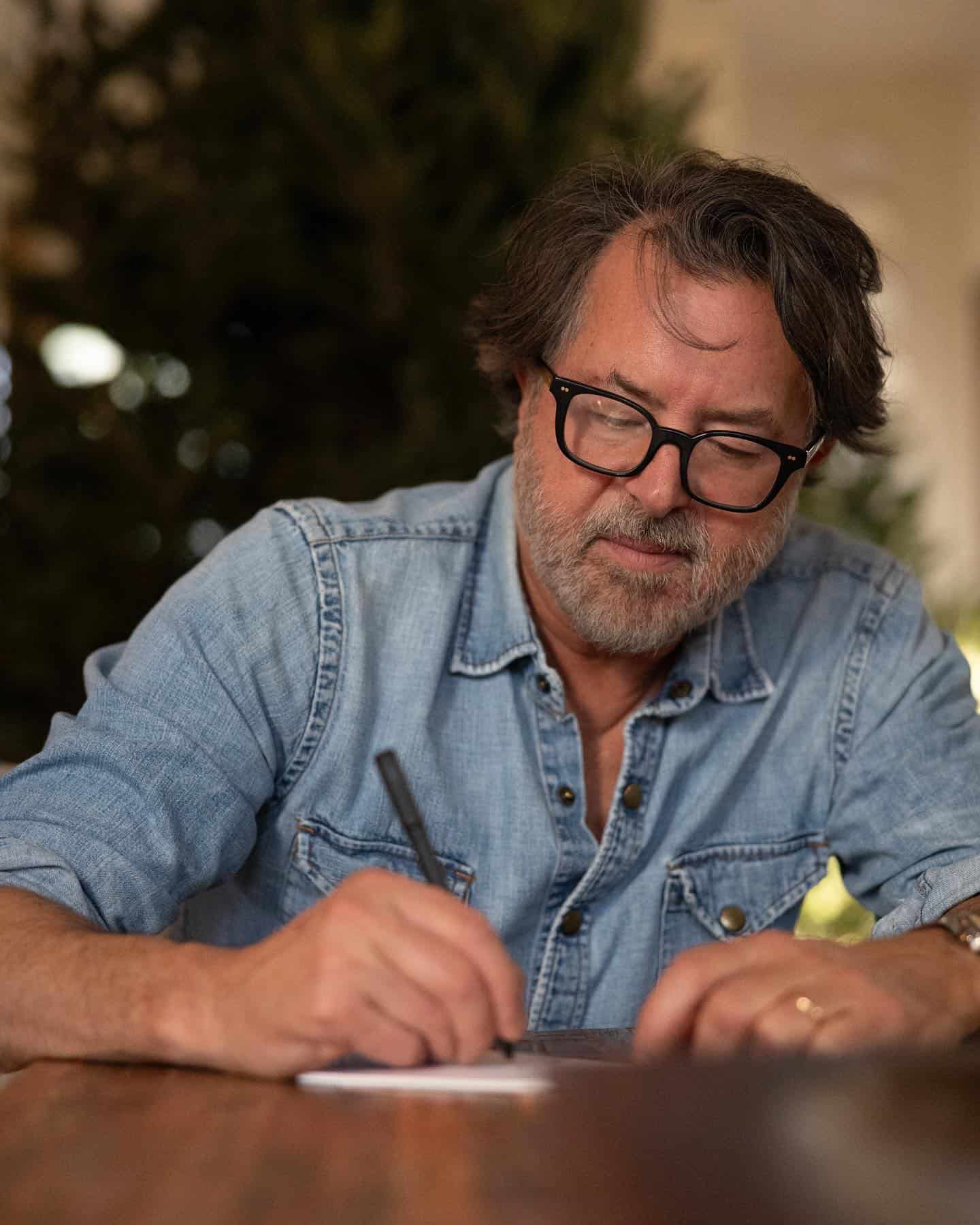 man in a denim shirt writing down a note