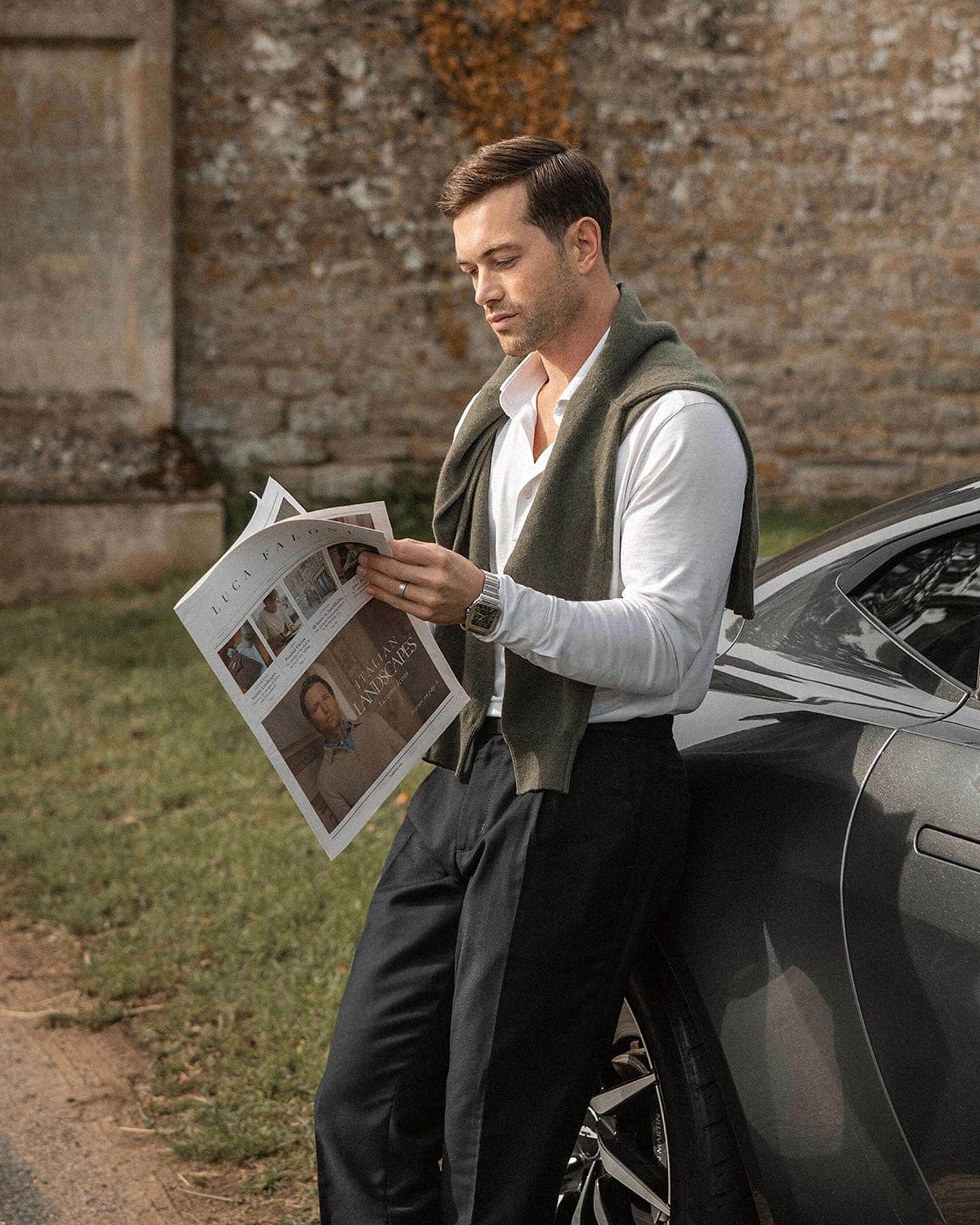 man leaning on a car while reading the papers