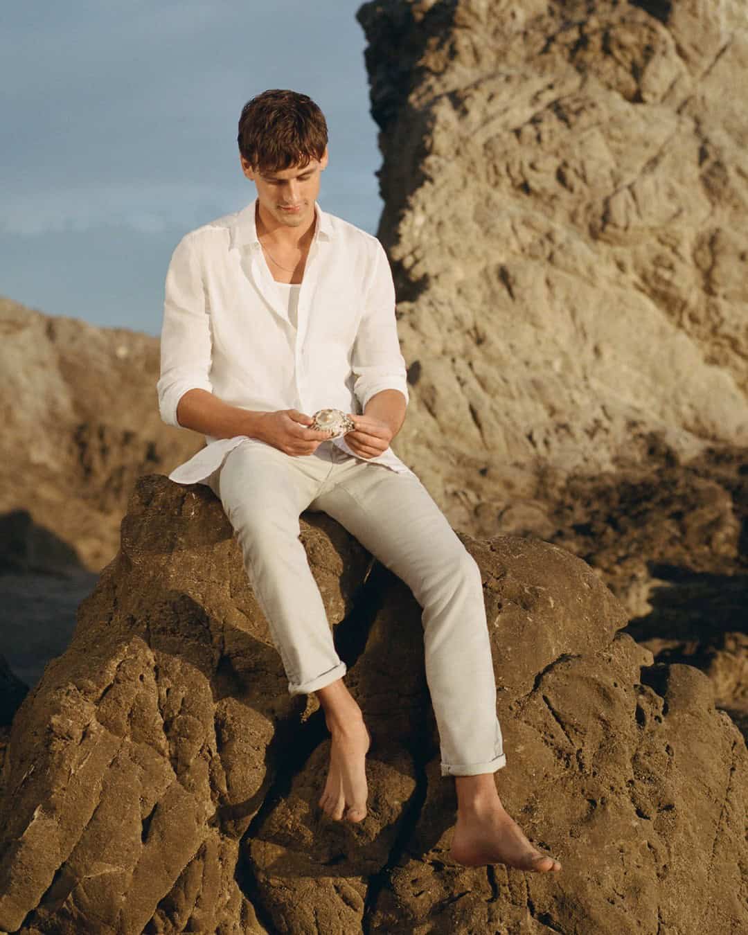 man sitting on the rocks wearing white shirt and jeans