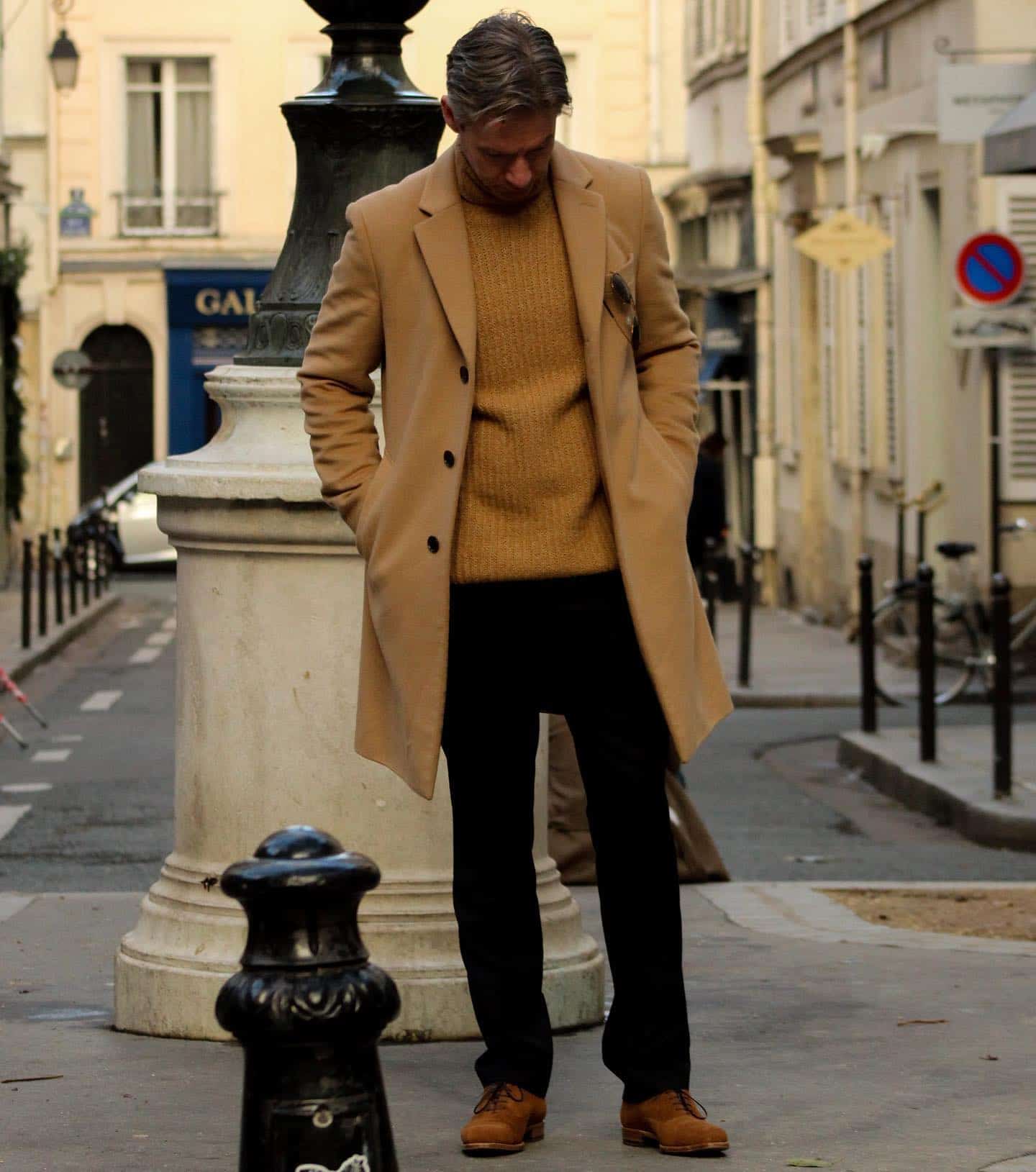 homem com um longo casaco marrom verificando seus sapatos
